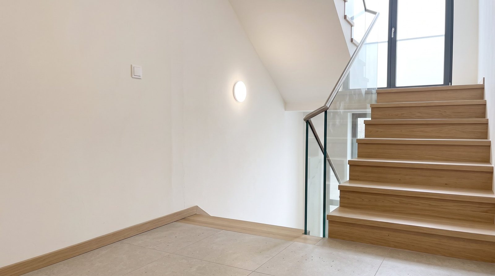 Modern saniertes Treppenhaus: helle Wände, Treppenstufen aus Eiche, Glasgeländer mit Edelstahlhandlauf, großformatige Bodenfliesen und bodentiefes Fenster