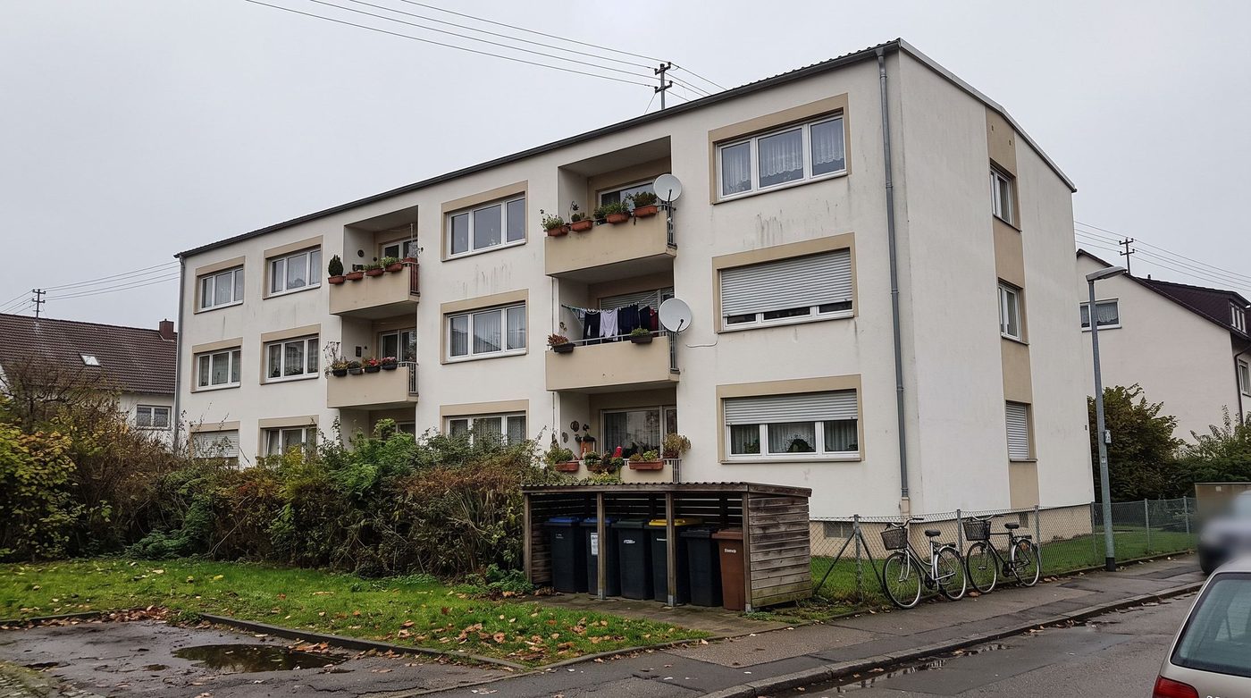 Saniertes Mehrfamilienhaus mit hellem Putz und Balkonen in einer Wohnstraße